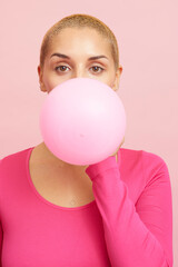 Young blond woman blowing pink balloon 