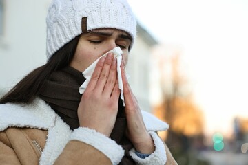 Woman with tissue blowing runny nose outdoors, space for text. Cold symptom - obrazy, fototapety, plakaty