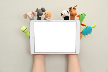 Person with animal puppets on fingers holding tablet against light background, closeup. Space for...