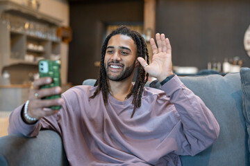 Man with dreads talking on video call while relaxing on sofa