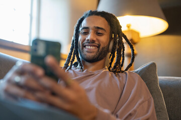 Man with dreads using phone and listening to music while relaxing on sofa