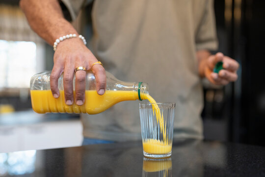 Close up of man pouring orange juice into glass  - Powered by Adobe