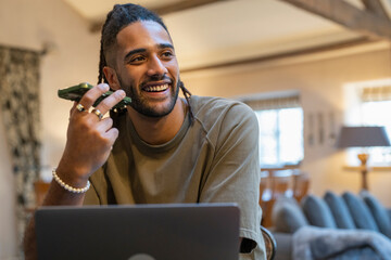 Man with dreads talking on phone and working on laptop at home © Cultura Creative