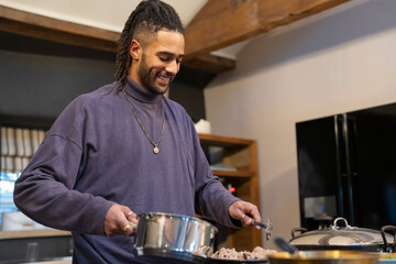 Smiling man preparing meal in kitchen  - obrazy, fototapety, plakaty