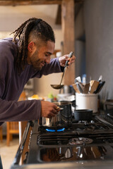 Man tastes food from pot in kitchen 