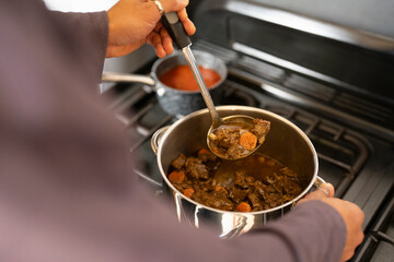 Man holds stew in ladle 
