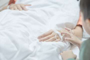 Woman lying in the hospital bed sleeping, Hand of her son holds it comfortingly. Soft focus. Copy...