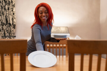 Smiling redhead woman setting table for dinner - obrazy, fototapety, plakaty