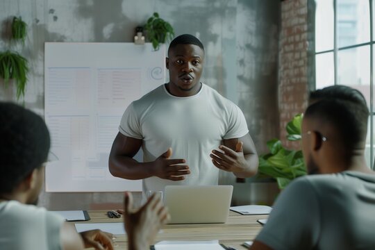 Confident young male African American project manager presenting management strategy, standing at meeting table, talking to team, explaining teamwork plan, work tasks