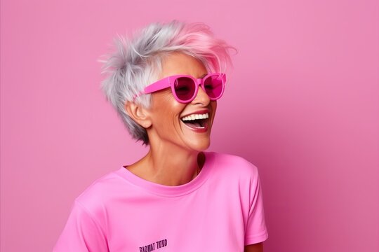 Smiling woman with pink hair and sunglasses on a pink background.