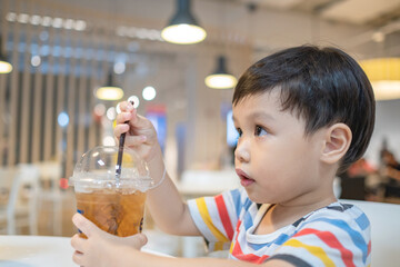 Little boy is sucking ice tea with straws in a glass with ice. Copy space.