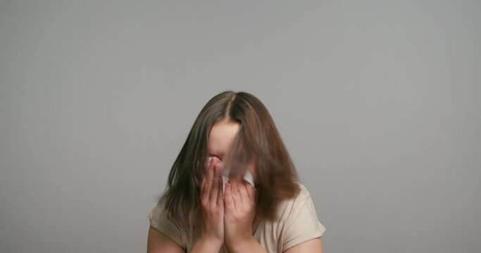 Young latin teen girl with allergy sneezing. Girl feeling sick having runny nose on gray background