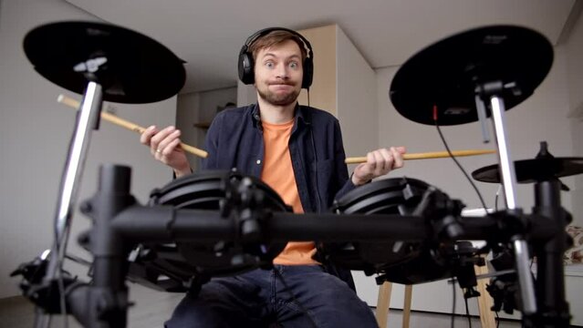 Confused man drummer beginner with headphones trying to play electric drum at home