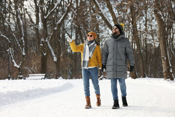 Fototapeta na wymiar Beautiful happy couple walking in snowy park on winter day