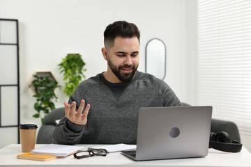 E-learning. Young man using laptop during online lesson at white table indoors