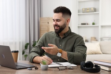 E-learning. Young man taking notes during online lesson at wooden table indoors