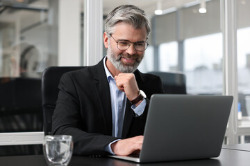 Smiling man working with laptop at table in office. Lawyer, businessman, accountant or manager