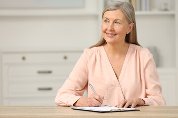 Smiling senior woman signing Last Will and Testament at wooden table indoors. Space for text