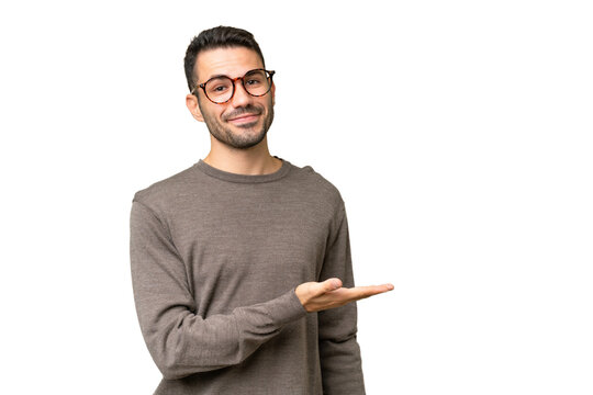 Young handsome caucasian man over isolated background presenting an idea while looking smiling towards