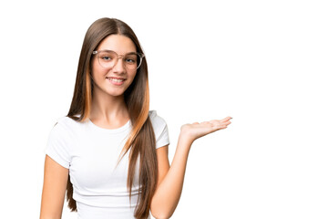 Teenager caucasian girl over isolated background holding copyspace imaginary on the palm to insert an ad