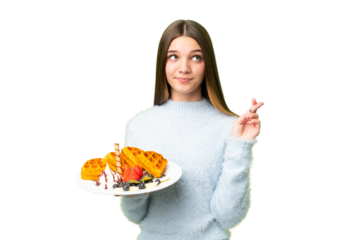 Teenager girl holding waffles over isolated chroma key background with fingers crossing and wishing the best