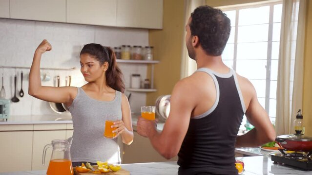 Joyful active fitness couples drinking nutritious orange juice after workout at kitchen by toasting - concept of healthy lifestyle, morning routine and relationship bonding