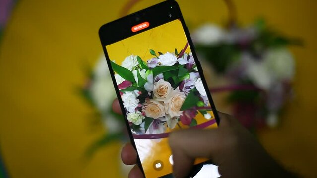 the hand holds the phone and takes a video of flowers bouquet