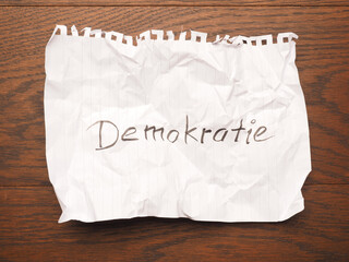 Wrinkled paper sheet with the German word democracy on a wooden table