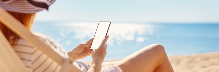 Woman sitting with smartphone in the chaise lounge on the sea beach.