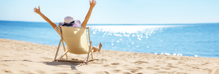 Happy woman sitting with raised hands in the chaise-lounge on the sea beach. - 733978932