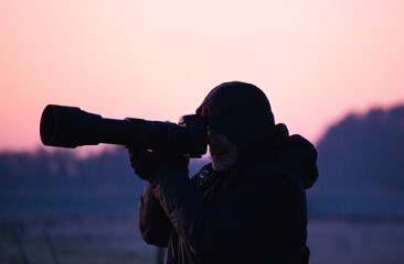 Photographer with a camera in the field at sunset. Silhouette