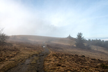 Noch ist der Dunst des Morgens nicht ganz verschwunden. Der Wanderweg zum Fliegerdenkmal, welches am Horizont zu erkennen ist liegt  in leichten Dunst . Am Himmel bricht langsam das Sonnenlicht durch