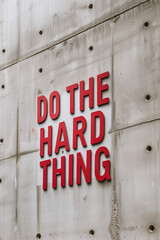 Old sign that says "Do the hard thing" on a rough concrete wall. Created with Generative AI technology