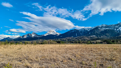 Scenic view of majestic snow capped mountain peak Mittagskogel in Karawanks, Carinthia, Austria. Landscape of Finkensteiner Moor covered by golden dry grass and reed. Idyllic hiking trail in spring