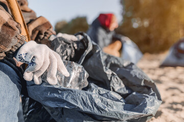 Close up shot of child in gloves collecting plastic bottles on the beach. Environmentalism,...