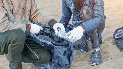 Unrecognizable young man picking up plastic trash with group of volunteers on the beach. Zero-waste concept. Recycling. Earth Day. Environment conservation