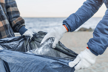 Close up of women collects plastic garbage in a garbage bag on the sea beach. Cropped shot of...