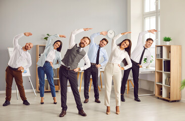 Happy young business people doing stretching sport exercises standing together in modern office....