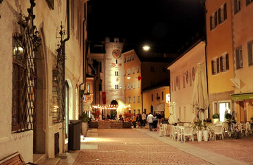 Fototapeta premium People walking at night in the center of Brunico.