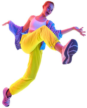 Happy young woman training, dancing in trendy sport outfit and sneakers looking at camera in neon light against transparent background. Concept of sport, fashion, active lifestyle, youth. Copy space