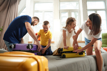 Parents help their children to packing clothes in living room at home before leaving for children's health camp. Joyful mood before trip. Concept of tourism, holiday, vacation, relaxation. Ad - obrazy, fototapety, plakaty