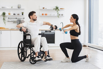 Female physiotherapist or wife showing mature male patient in wheelchair how to exercise with...