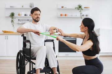 Professional physiotherapist in sportswear helping adult man with a disability in wheelchair to...