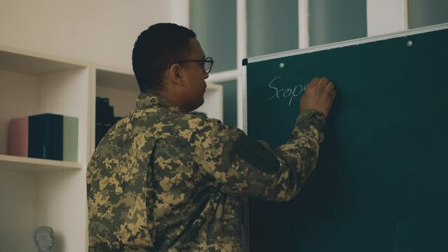 Army officer teaching military academy cadets, writing subject on blackboard