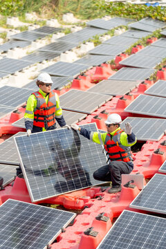 Vertical image of two professional technician workers hold solar cell panels during installation or set up to the system and they work over water reservoir area.