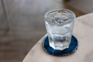Glass of water with ice cubes on marbled table at restaurant with copy space.