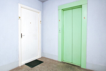 Green old elevator in hallway and door to apartment