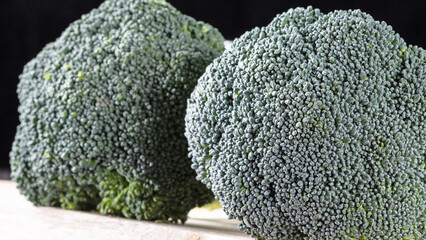 Fresh green broccoli florets up close on a white cutting board against a black background.