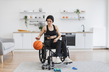 Cheerful beautiful woman with mobility impairment dribbling ball in studio apartment on weekend....