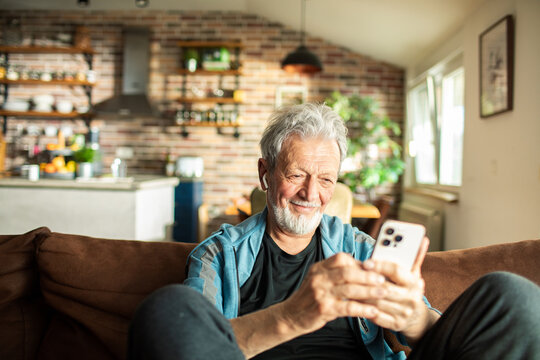 Senior man using a smartphone on the sofa at home